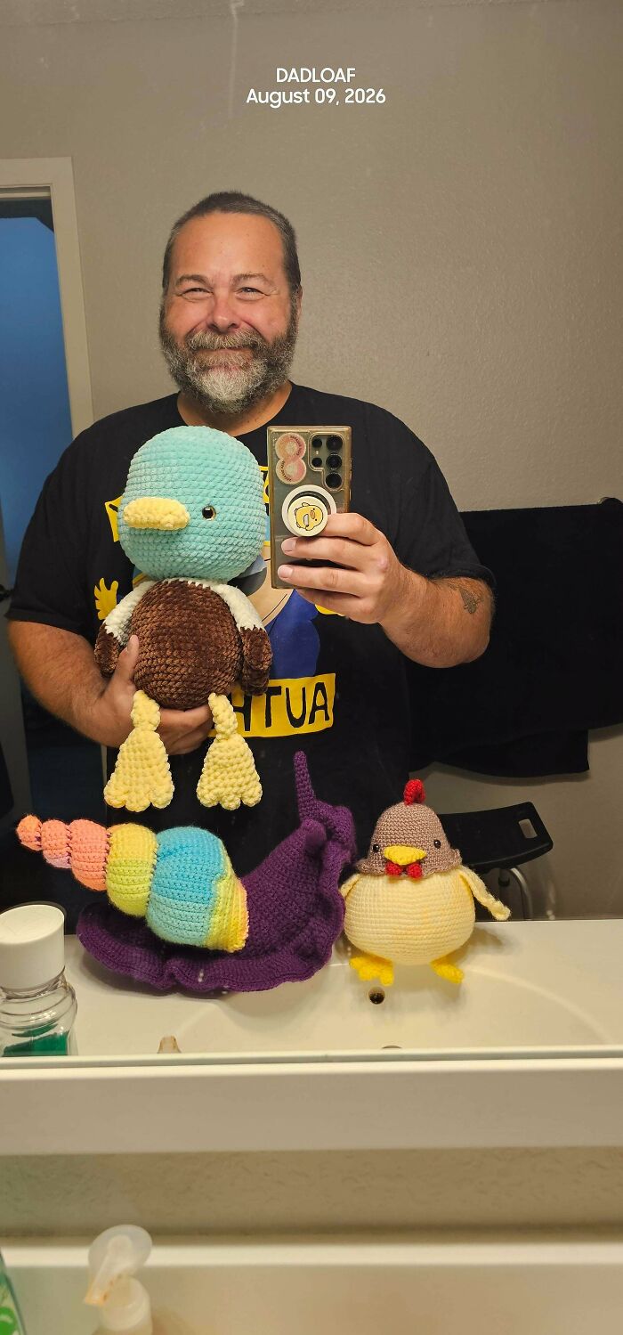 Man holding crochet plush toys of duck, caterpillar, and chicken