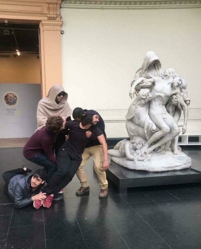 A group of men poses next to a sculpture, mimicking the positions of the figures in the artwork, a pic people cannot explain.