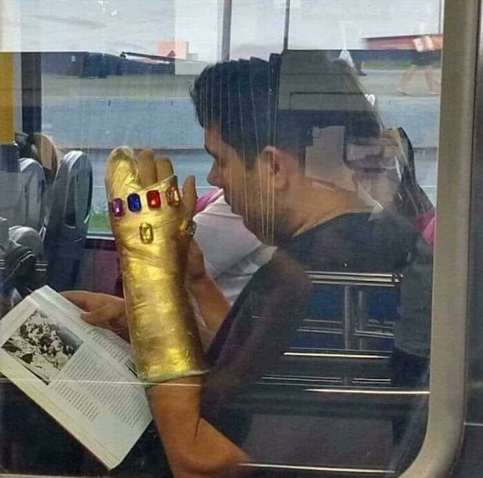 A man wearing a golden Infinity Gauntlet cast while reading a book on a bus, one of the pics people cannot explain.