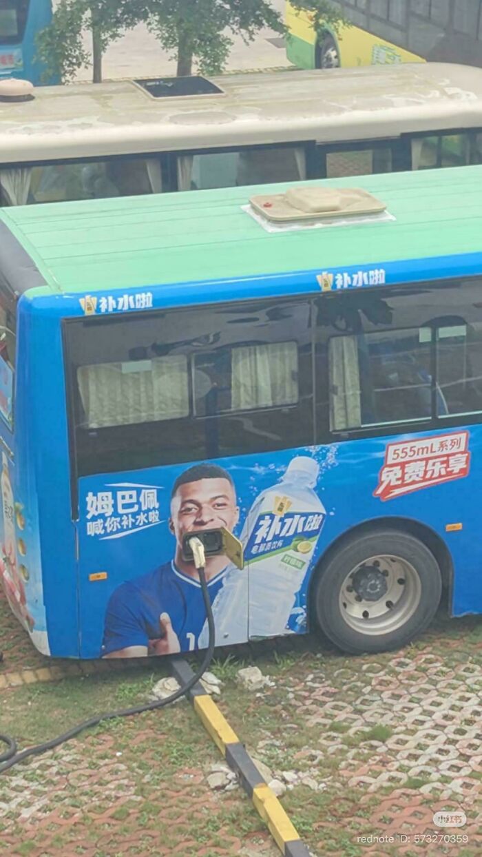 A bus with a large advertisement for a drink, featuring Kylian Mbappe inexplicably holding a charger connected to the bottle.