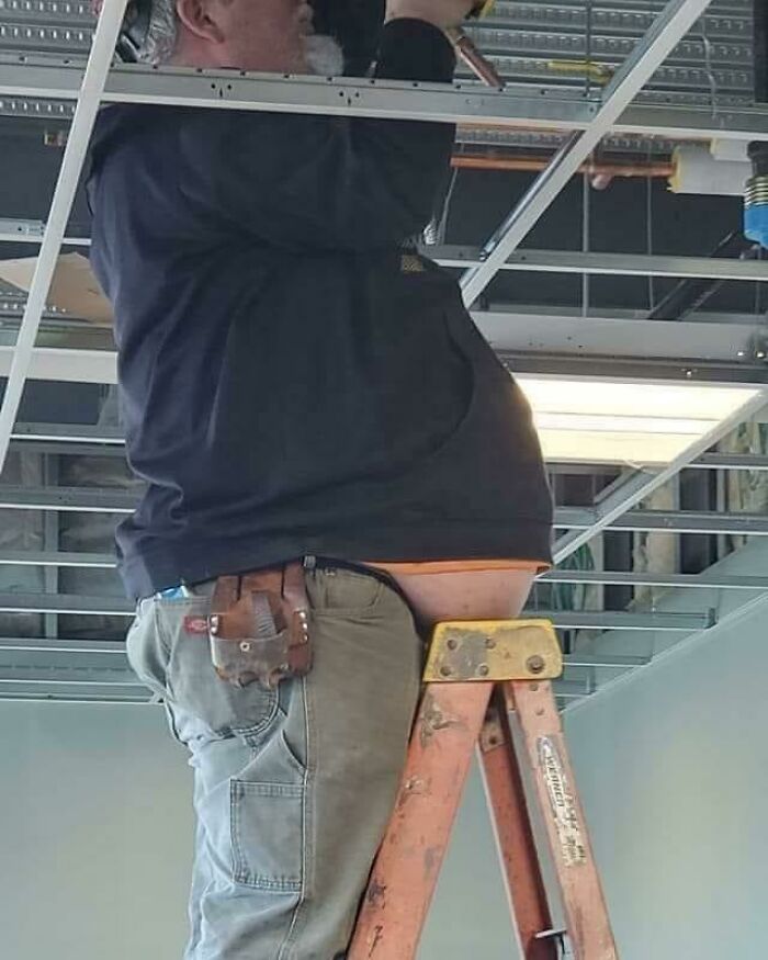 A construction worker on a ladder, unable to explain why his stomach rests on the top rung, creating a funny and unforgettable image.