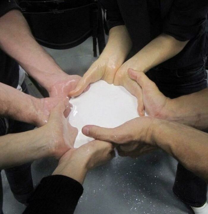 Many hands cupped together holding a white liquid, an image that people cannot explain or forget.