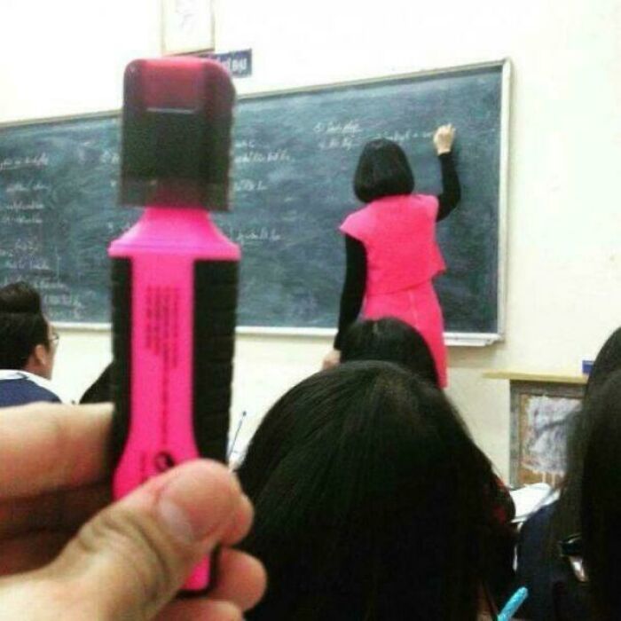A person holding a pink marker in the foreground, perfectly aligned with a teacher in a matching pink dress writing on a blackboard. Cannot Explain Pics.