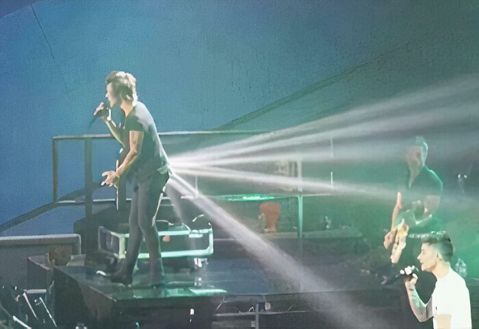 A performer on stage with a microphone, surrounded by bright lights, creates an optical illusion of light streaming from his back, a confusing pic.