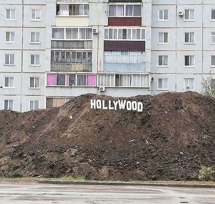 A small 'HOLLYWOOD' sign on a dirt mound in front of an apartment building, an unexplainable pic.