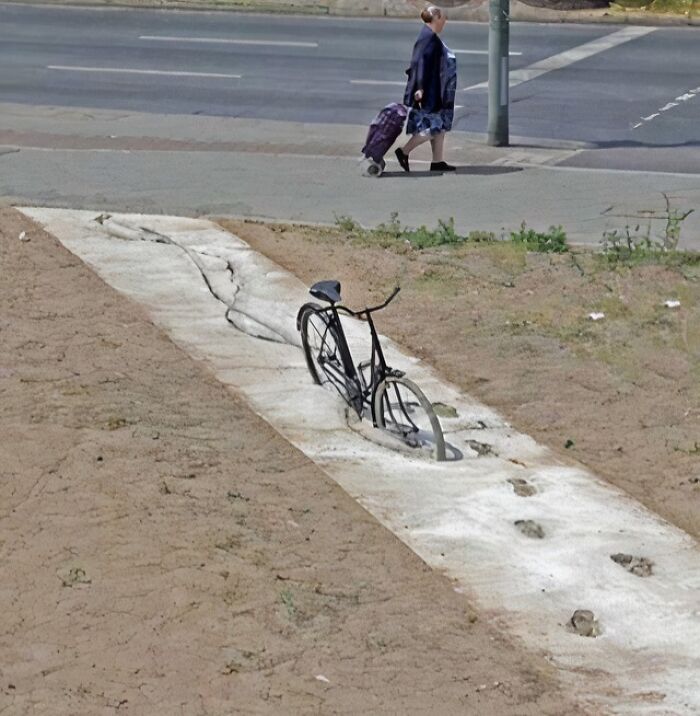 A bicycle embedded in concrete with footprints, an unexplainable pic that people cannot explain.