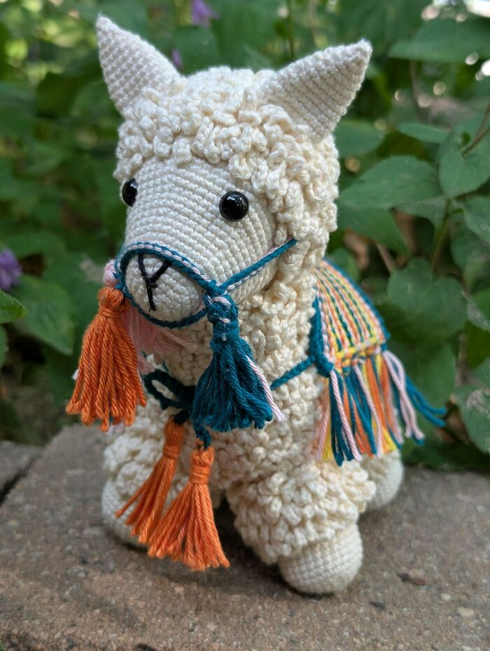 Crochet llama stuffed toy with tassels sitting outdoors on stone