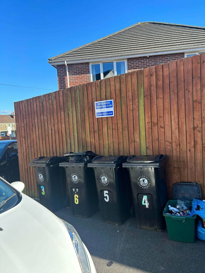 Four bins blocking a reserved parking spot, highlighting inconsiderate neighbors and parking issues.