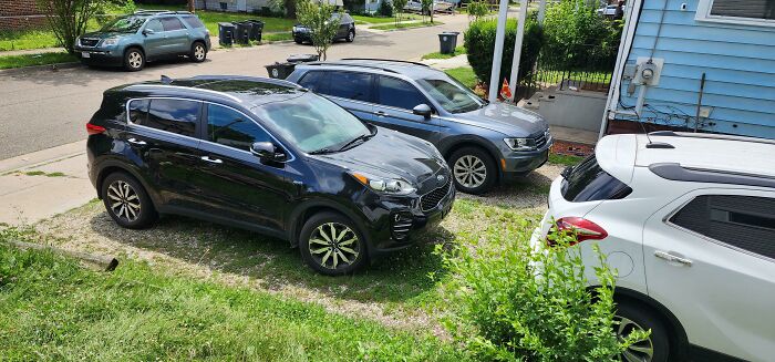Three cars poorly parked on a lawn and driveway, demonstrating a lack of common sense among neighbors.