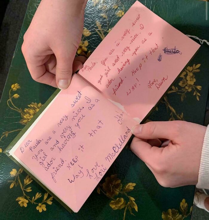 Two hands holding open a pink handwritten note, representing a personal piece of ephemera from the past.