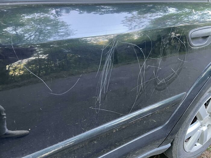 A black car door heavily scratched with white marks, leaving parents thinking "Why did I sign up for this?"