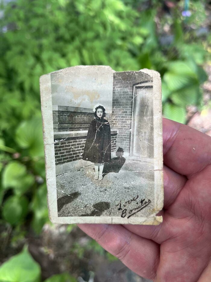 A faded black and white photo of a girl in a coat held in a hand, an old piece of ephemera showing how much the past has changed.