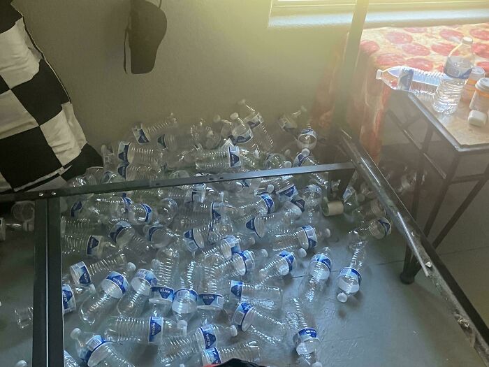 Numerous empty plastic water bottles scattered on the floor next to a bed, making becoming a cat lady appealing.