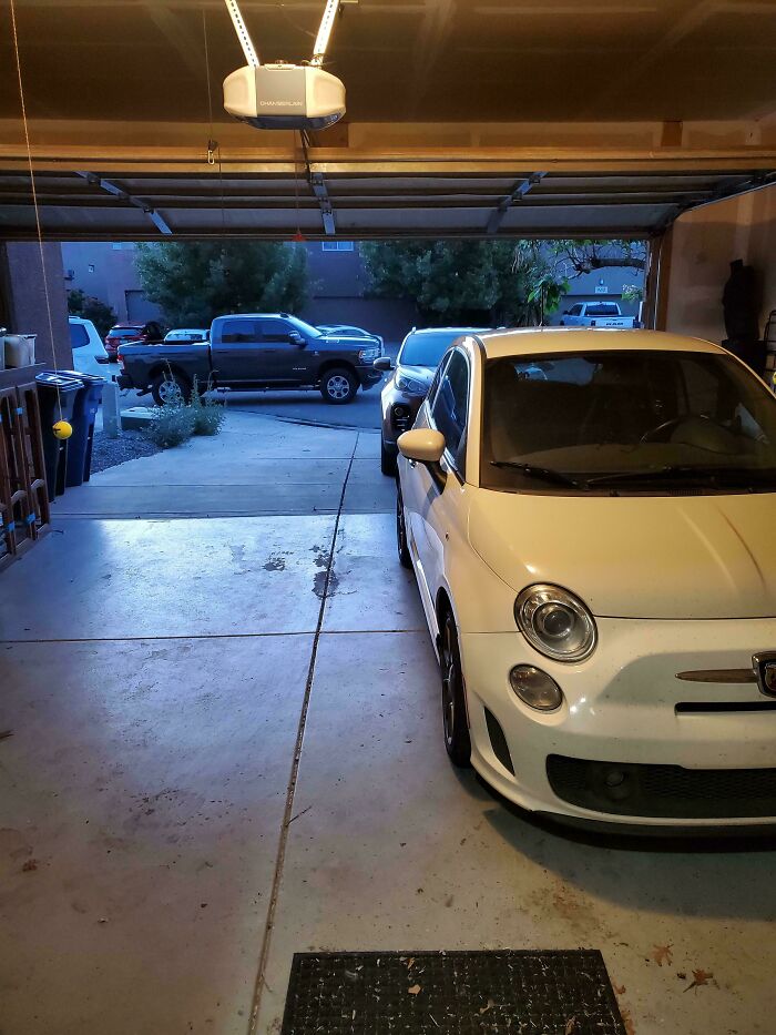 A white car in a garage with a black truck visible outside, showcasing neighbor parking issues.