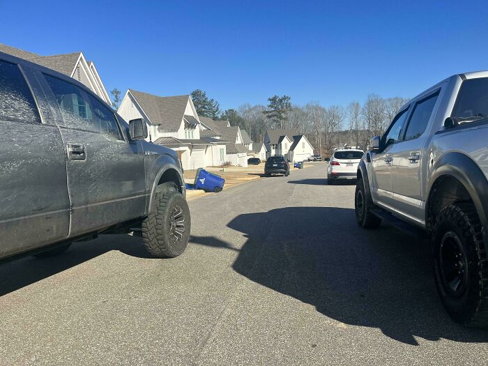 Two large trucks parked on opposite sides of a narrow street, illustrating poor parking by neighbors.
