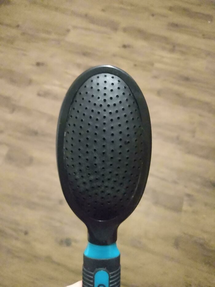 A close-up of a black and blue hairbrush with a textured surface, making parents think: Why Did I Sign Up For This?
