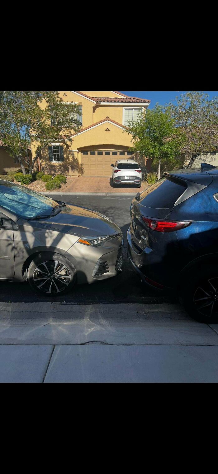 Two cars parked bumper-to-bumper on a street in front of a house, demonstrating poor parking by jerk neighbors.