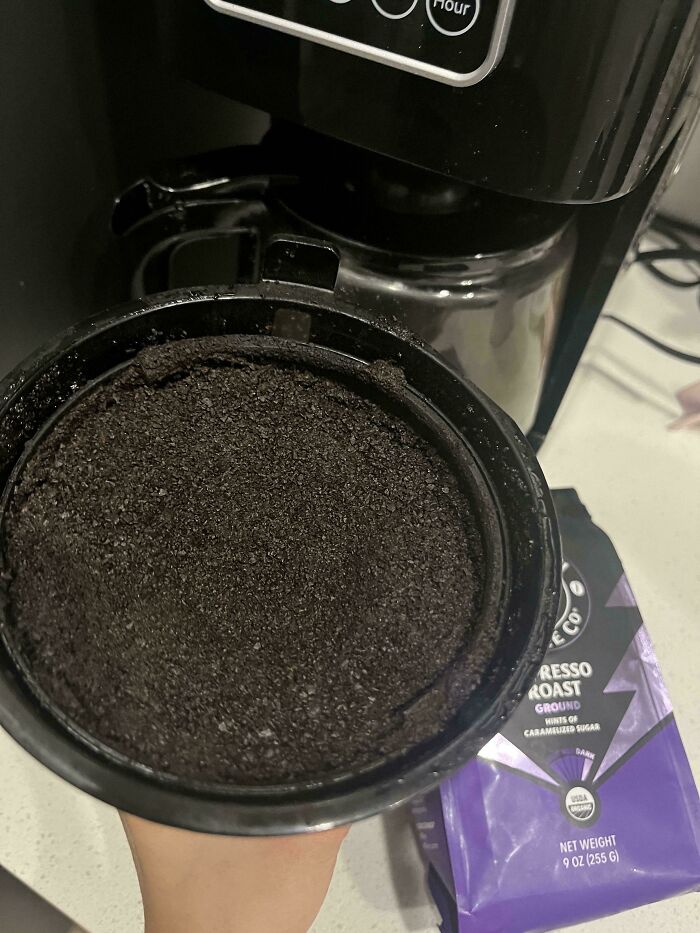 A coffee maker's filter filled to the brim with used coffee grounds, a messy habit that makes becoming a cat lady look attractive.