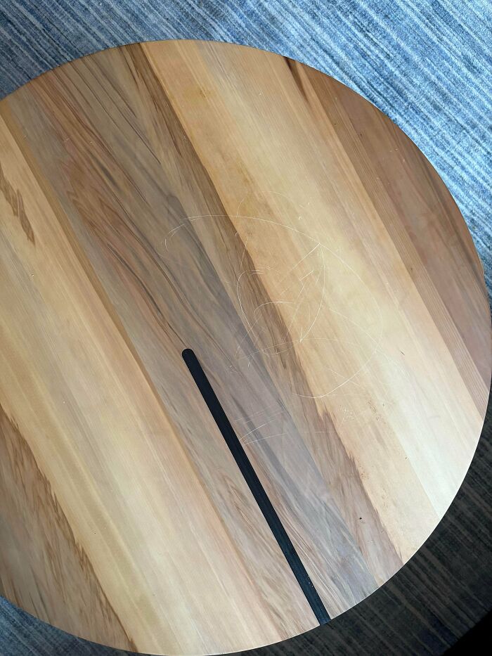 A round wooden table with visible scratches on its surface, reflecting a common parenting challenge.