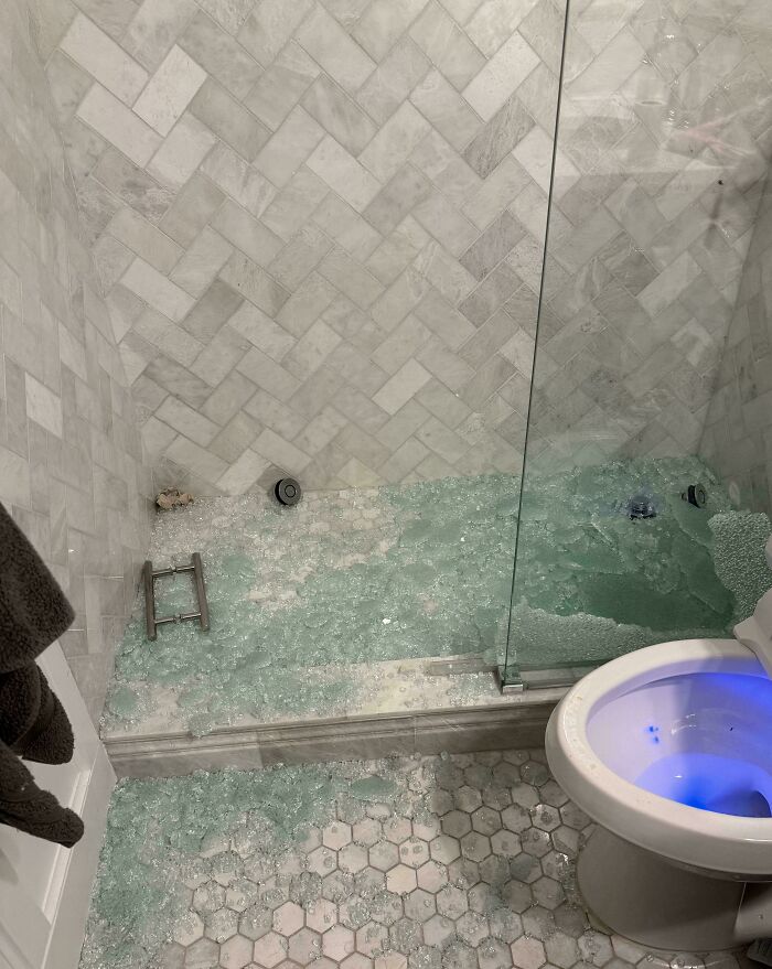 A bathroom with a broken glass shower door and shattered glass on the floor, illustrating a parents dilemma.