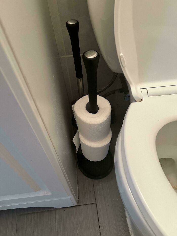 A toilet paper holder with rolls stored incorrectly on the plunger handle, highlighting disorganized tendencies that make becoming a cat lady look attractive.
