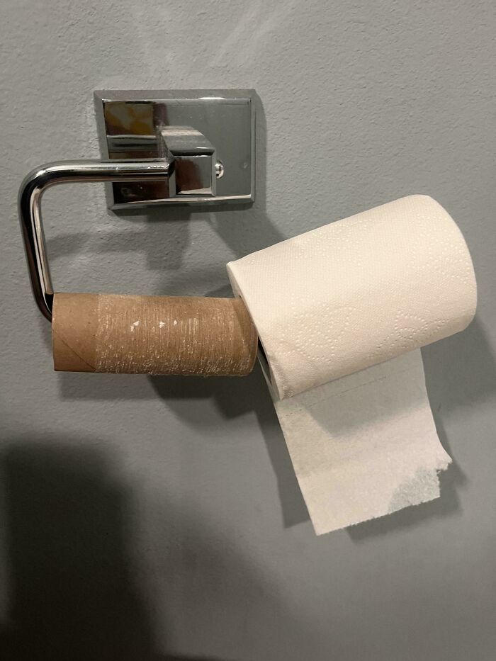 An empty toilet paper roll on the holder with a new roll placed precariously on top, promoting the cat lady lifestyle.