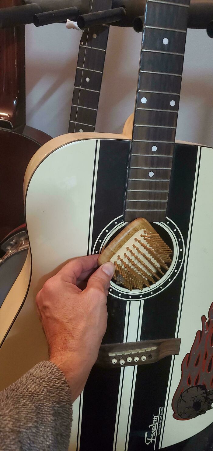 A hand removes a child's hairbrush from a guitar soundhole, showing parents finding kids objects in odd places.
