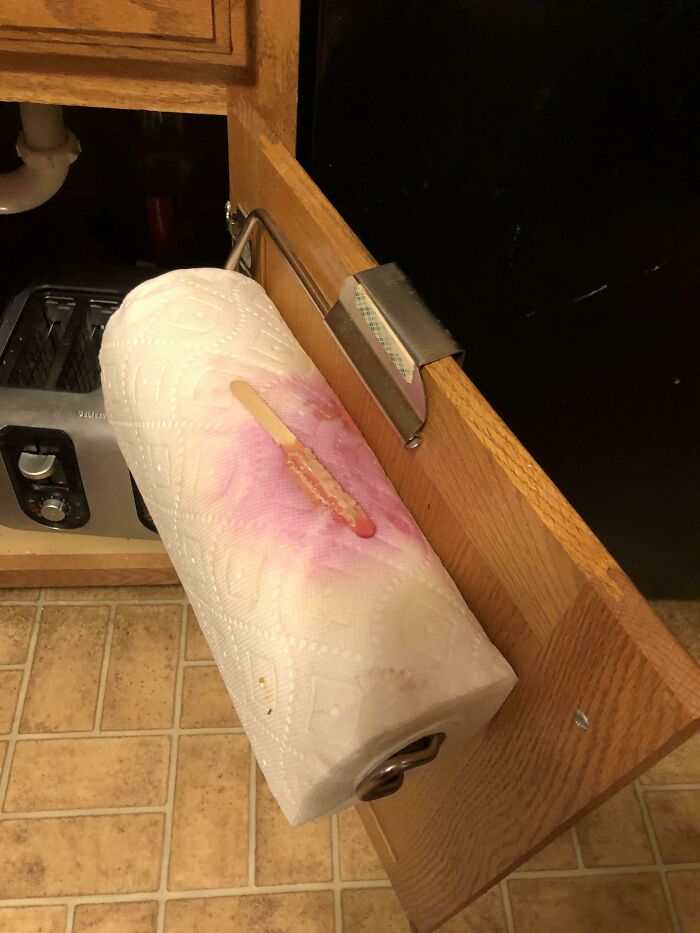 A melted popsicle on a paper towel roll on a cabinet highlights parents' daily struggles and cleaning.