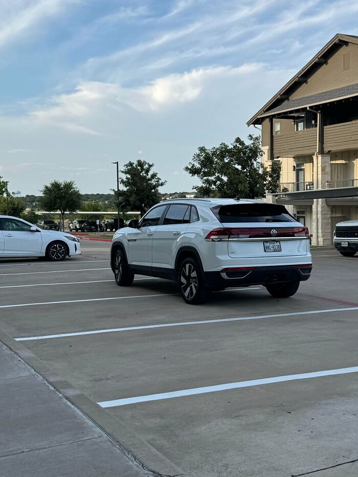 A white SUV, belonging to a jerk neighbor, is parked diagonally across two parking spaces in a lot.
