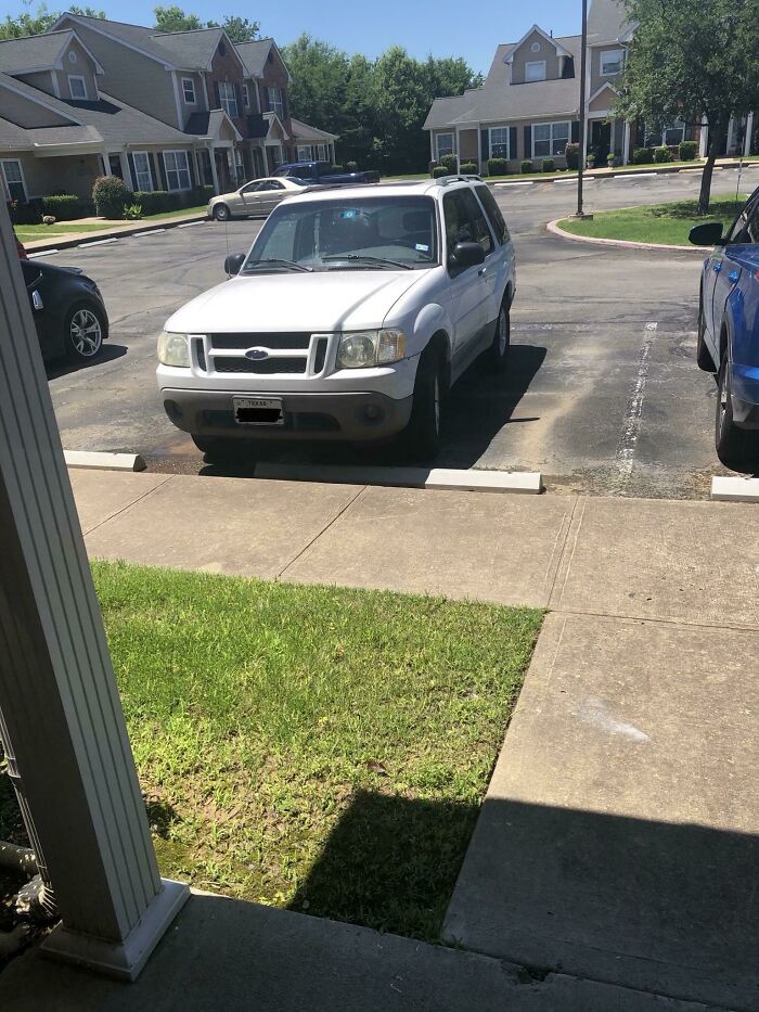 A white SUV, belonging to a jerk neighbor, is parked over the sidewalk and encroaching on the grass.