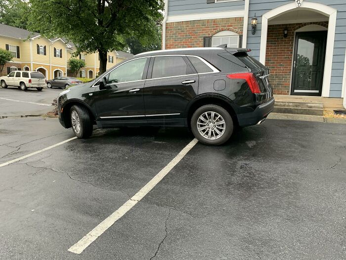 A black SUV parked incorrectly across a parking space line, an example of neighbors bad parking.