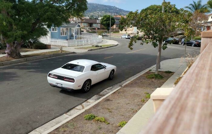 A white sports car parked far from the curb on a residential street, showcasing poor parking by neighbors.
