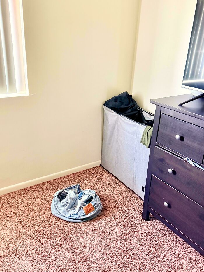 Jeans on the floor next to a laundry hamper, illustrating a common scenario that makes becoming a cat lady appealing.