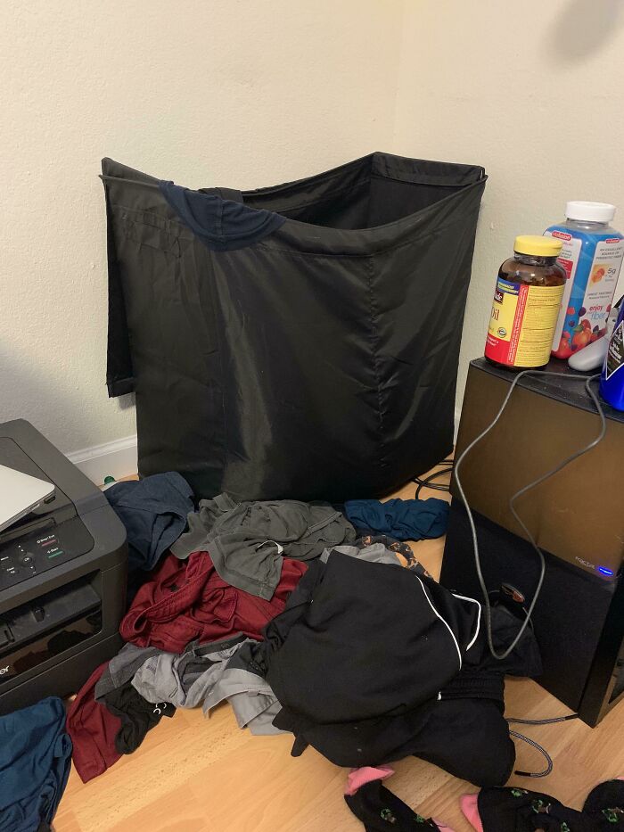 Piles of clothes on the floor next to an overflowing laundry hamper, highlighting men in relationships and the cat lady allure.