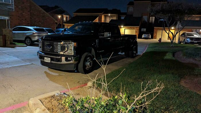 A large black pickup truck illegally parked on a fire lane next to a residential building at night, highlighting bad parking.