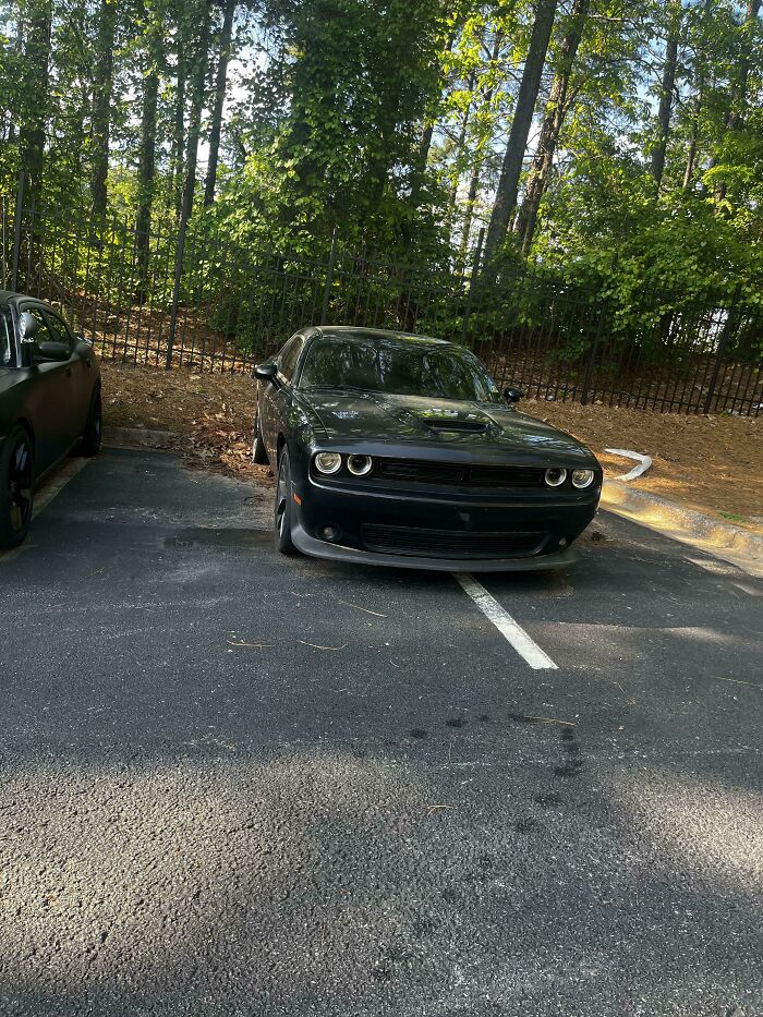 A black car poorly parked, taking up two parking spots, an example of jerk neighbors parking.