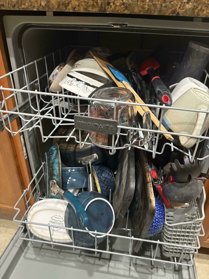 A full, disorganized dishwasher with dishes and utensils, making becoming a cat lady look more attractive.
