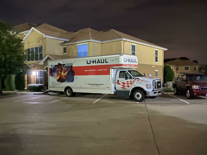 A large U-Haul moving truck occupying multiple parking spots in an apartment complex at night, demonstrating bad parking.
