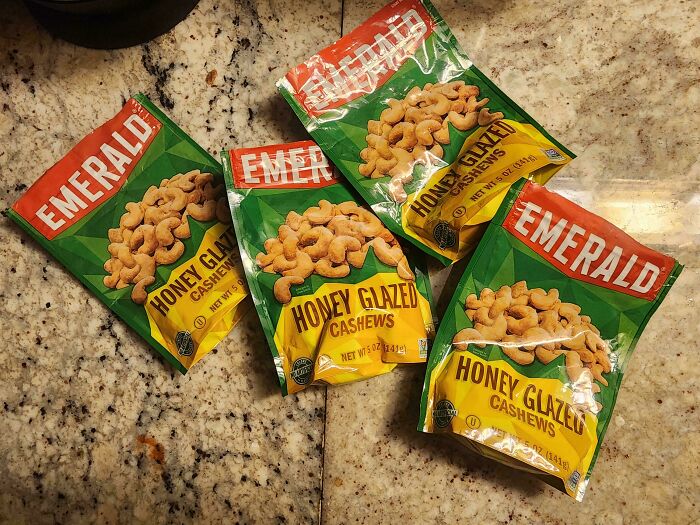 Four bags of Emerald Honey Glazed Cashews, representing a man in relationships and a cat lady. The bags are spread out on a speckled countertop.