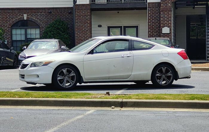 A white car poorly parked across two parking spots, blocking common sense parking etiquette from jerk neighbors.