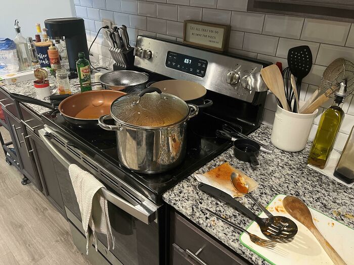 A dirty kitchen counter with pans and dishes, making becoming a cat lady look more attractive.