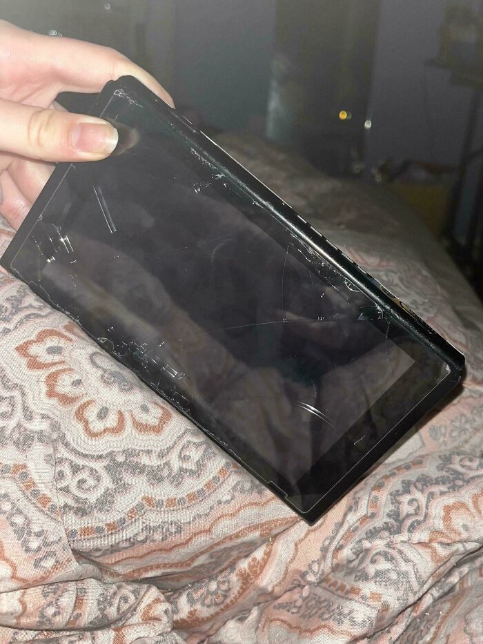 A hand holding a severely cracked and damaged portable gaming device, symbolizing relationship damage.