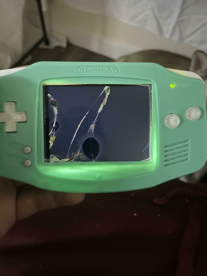 A close-up of a mint green Nintendo Game Boy Advance with a cracked screen.