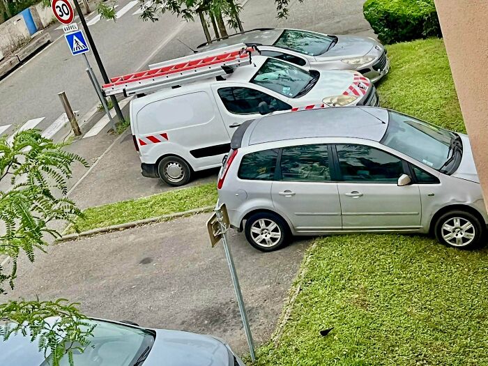 An urgent parking lesson for neighbors, with cars parked haphazardly on a grassy median and sidewalk.