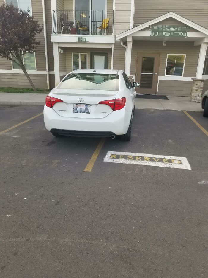 A white car poorly parked across a reserved parking spot, demonstrating a neighbor's bad parking.