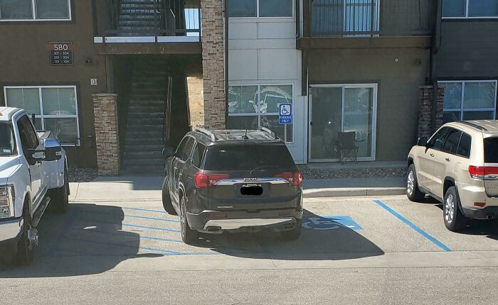 A black SUV poorly parked across two disabled parking spaces, showing a lack of common sense and parking etiquette.