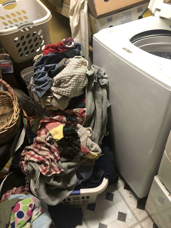 A pile of dirty clothes next to a washing machine, making becoming a cat lady look more attractive.