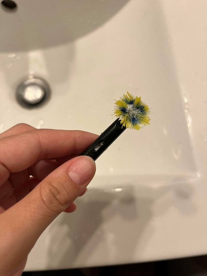 A worn-out toothbrush head is held over a sink, highlighting how men in relationships can be less attractive.