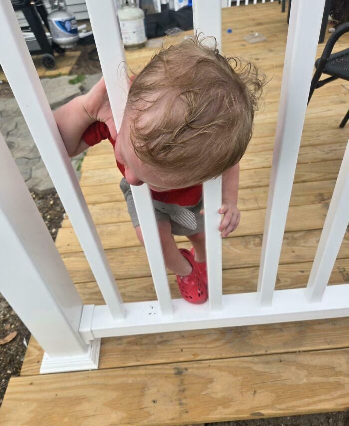 A small child with blonde hair stuck between white deck balusters, highlighting moments for parents.