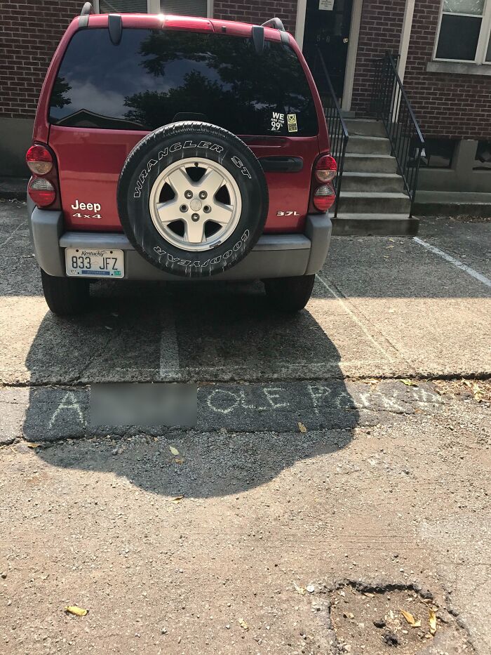 A red Jeep Wrangler demonstrating an urgent parking lesson, parked over a chalk message about poor parking.